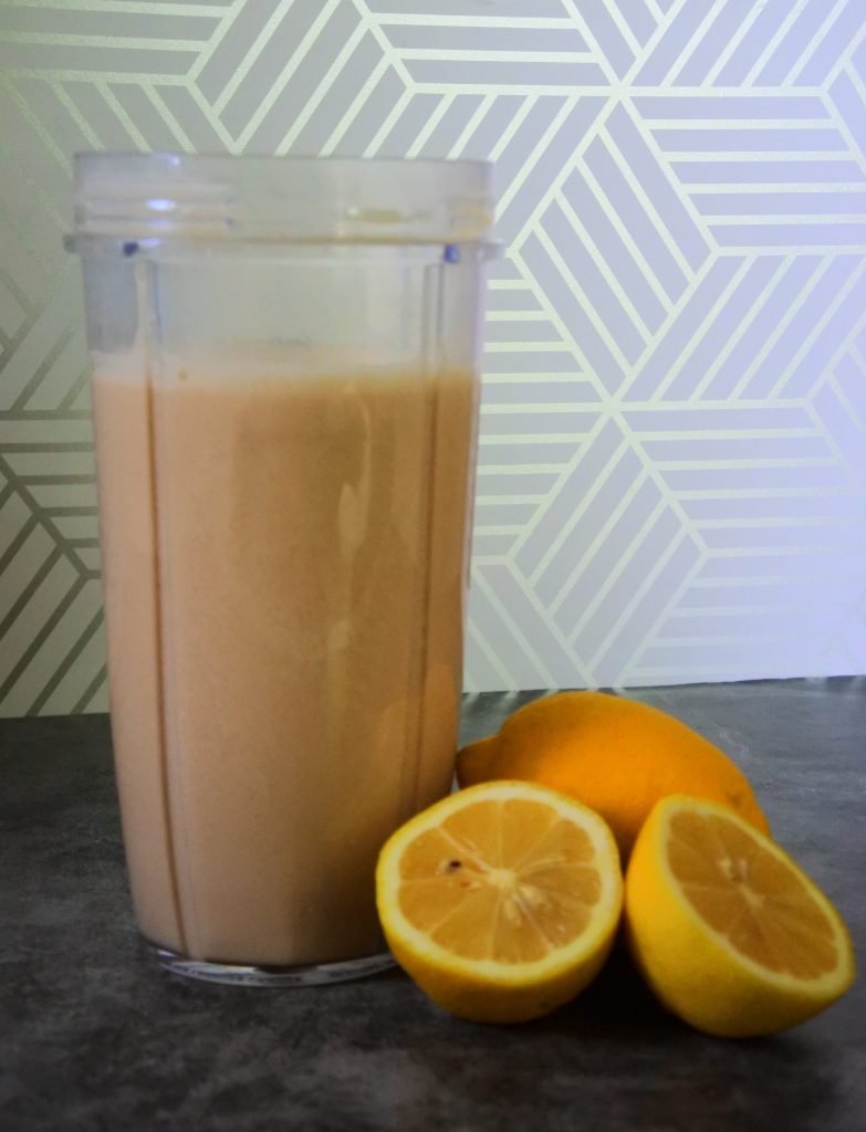 A close up image of a blended together creamy dreamy lemonade surrounded by fresh lemons