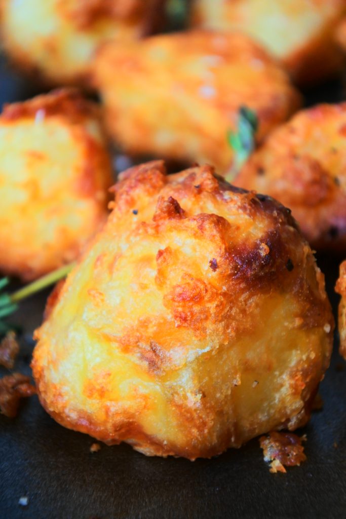 A close up image of crispy roast potatoes on a tray topped with flaky salt and fresh herbs