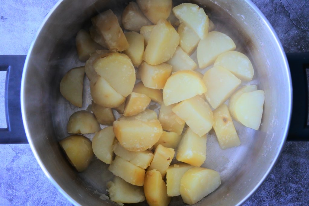 An overhead image of a pot of boiled potato chunks being left to "dry out" and let some steam dissipate.
