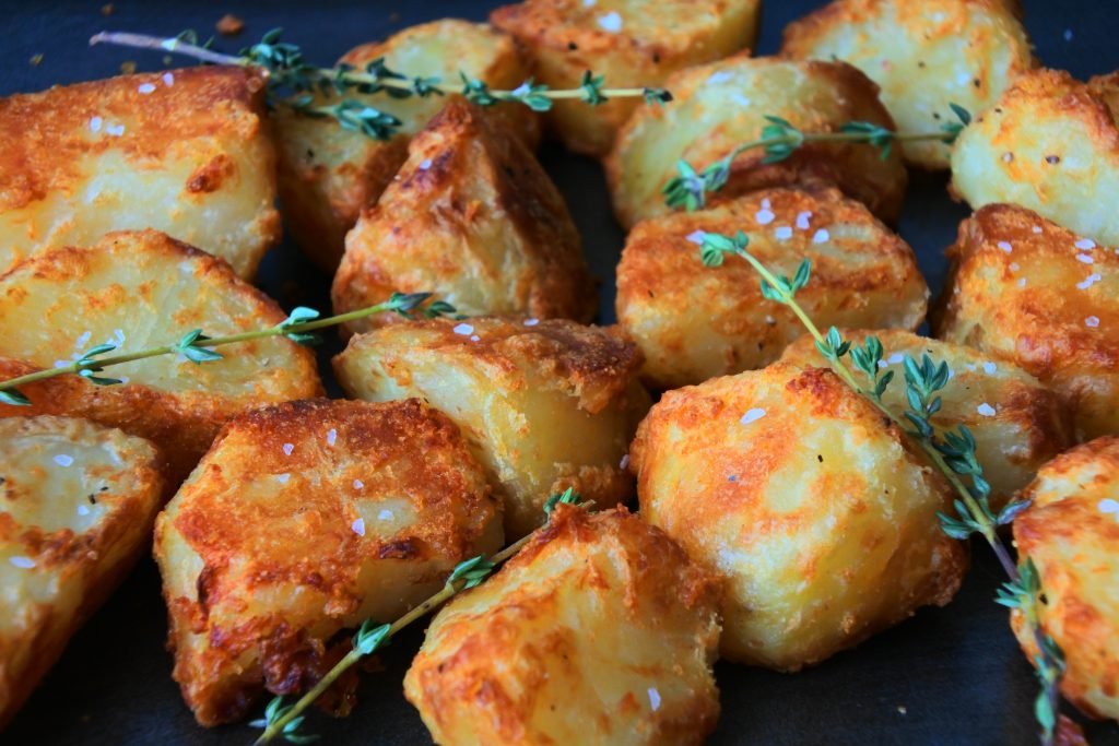 A close up image of crispy roast potatoes on a tray topped with flaky salt and fresh herbs