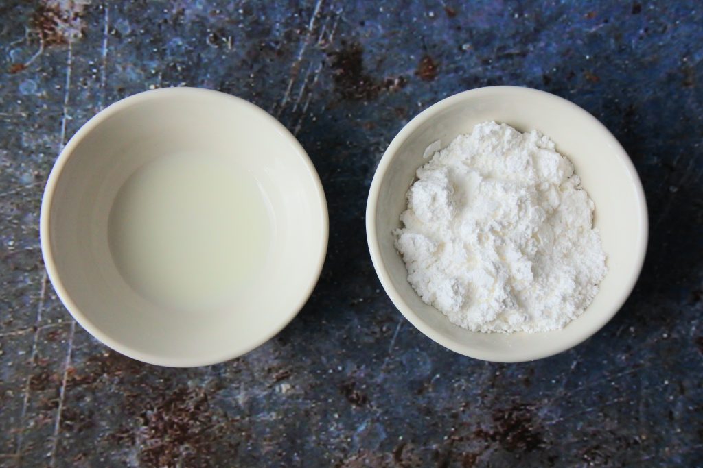 An overhead image showing two small dishes; one with whole milk and the other with icing sugar