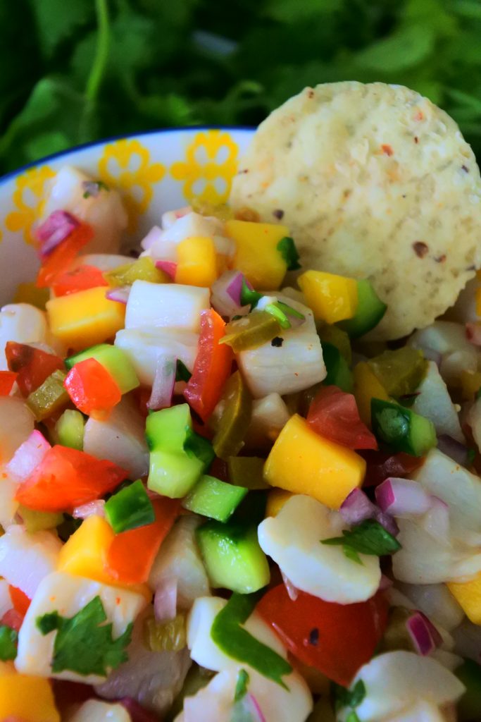 A close up image of a bowl of fresh scallop ceviche with a single tortilla chip ready to scoop into it