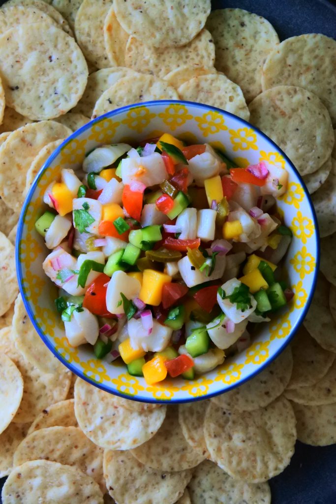 An overhead image of fresh scallop ceviche in a patterned bowl surrounded by tortilla chips