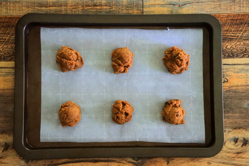 An overhead image of a parchment-lined tray of six scoops of gluten-free toffee chocolate chip cookie dough