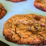 An angled image of a toffee chocolate chip cookie on a parchment-lined tray