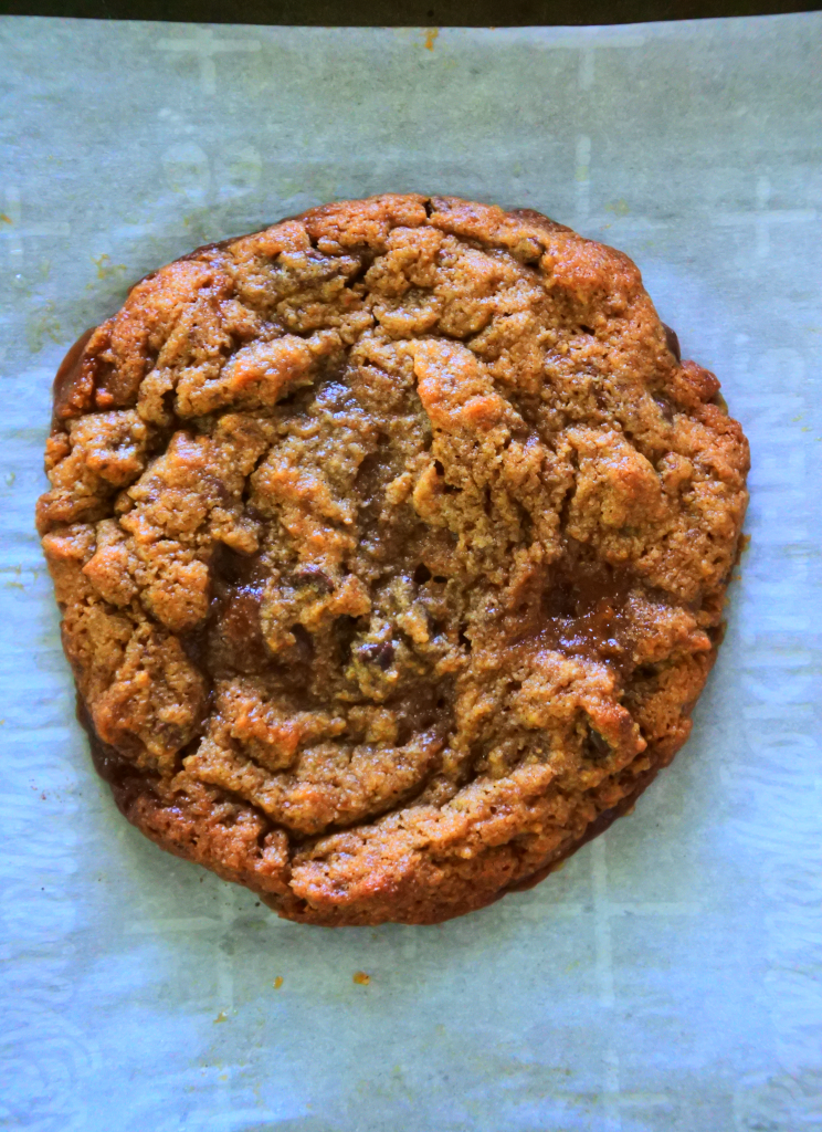 An overhead image of a toffee chocolate chip cookie on a parchment-lined tray