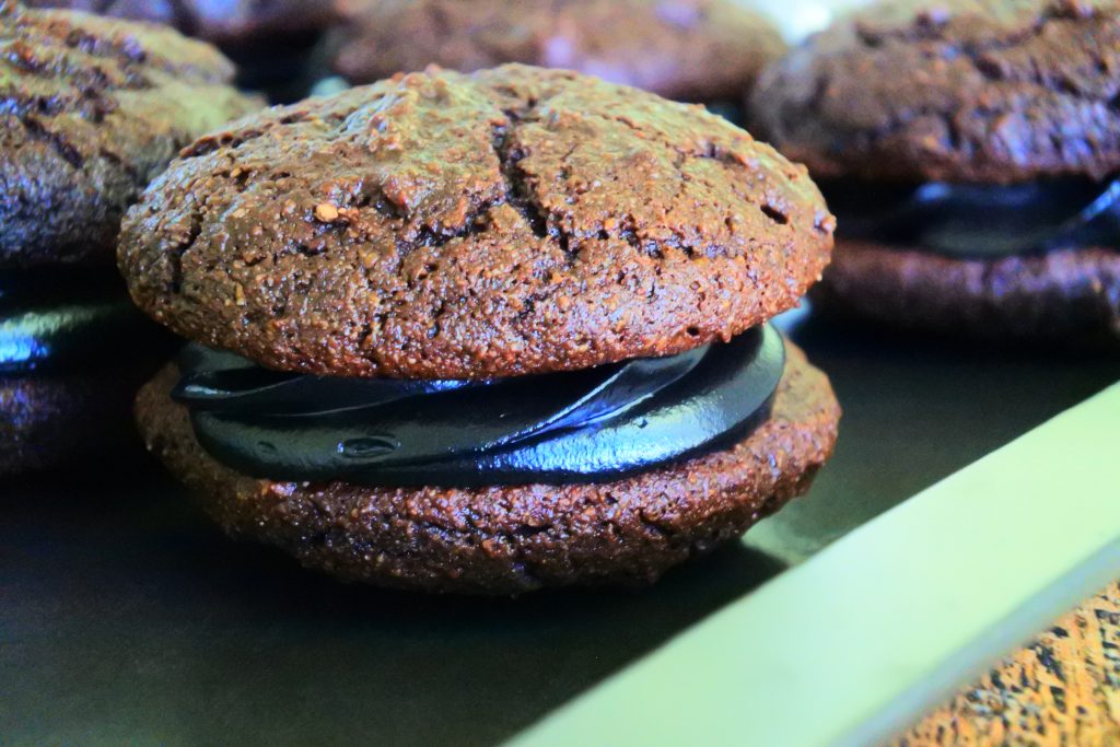 A close up image of chocolate whoopie pies with a black cocoa filling on a tray