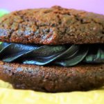 A head on close up image of a chocolate whoopie pie with a black cocoa filling