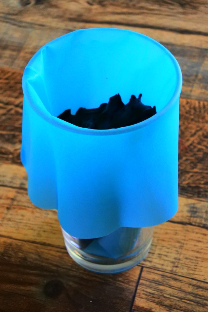 An angled image showing a piping bag slipped over a glass and filled with black cocoa frosting