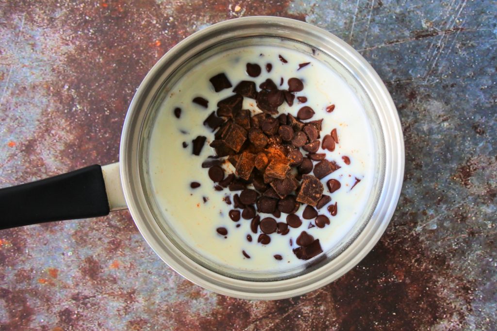 An overhead image of a small sauce pan with steaming milk with chocolate and spices added in and left to melt together