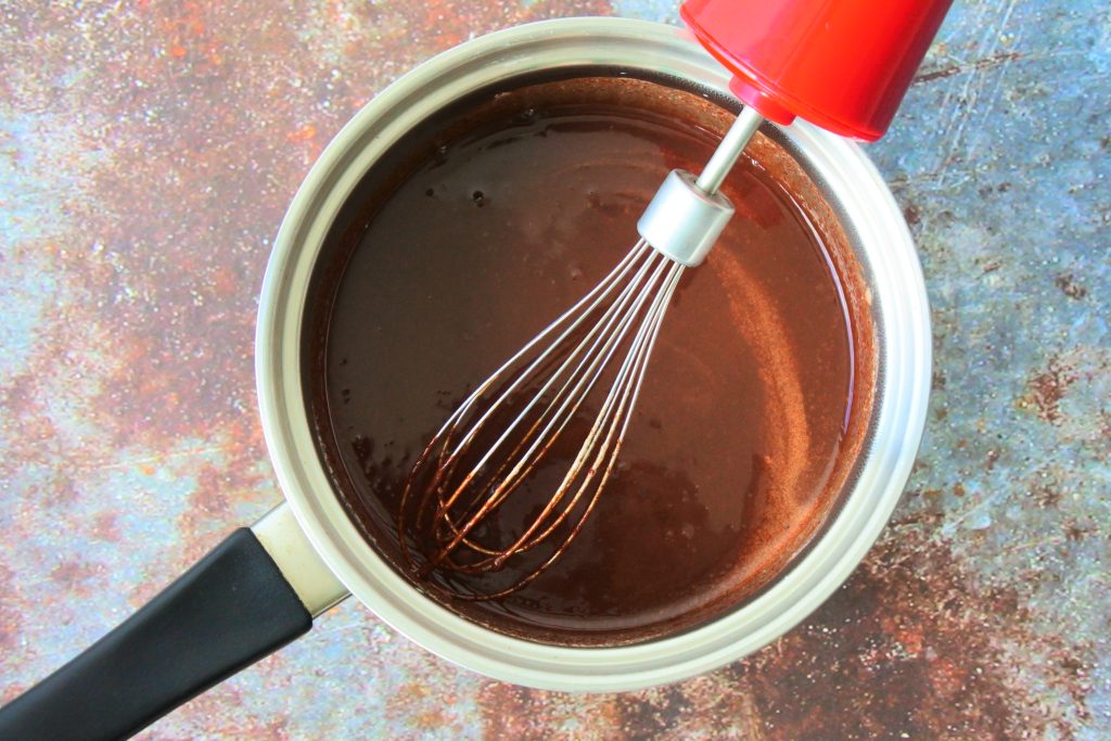 An overhead image showing a saucepan of a warm melted chocolate mixture with a whisk in it