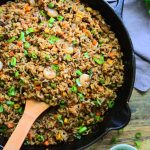 An overhead image of a skillet of shrimp fried rice on a wooden countertop with a small dish of chopped spring onions