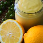 An angled image of a jar of lemon curd with fresh lemons around it