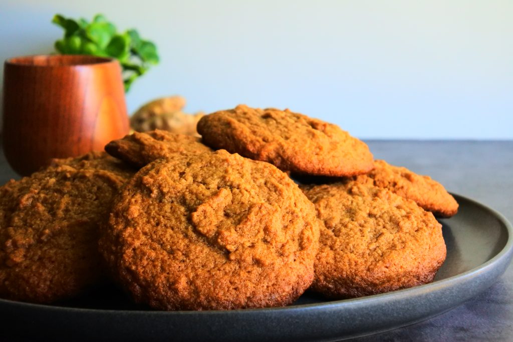 A close up image of a plate of freshly baked soft gluten free gingerbread cookies on a plate with a cup of milk and fresh spices in the background