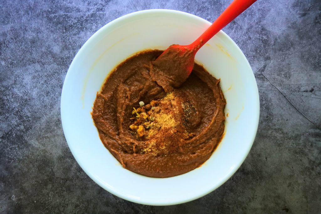 An overhead image of spices being added to the wet ingredients of a gluten free gingerbread cookie dough