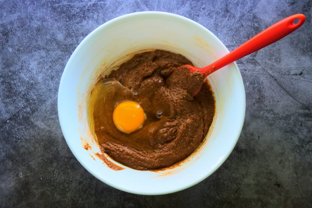 An overhead image of an egg being added to wet ingredients being mixed together for a gluten free gingerbread cookie dough