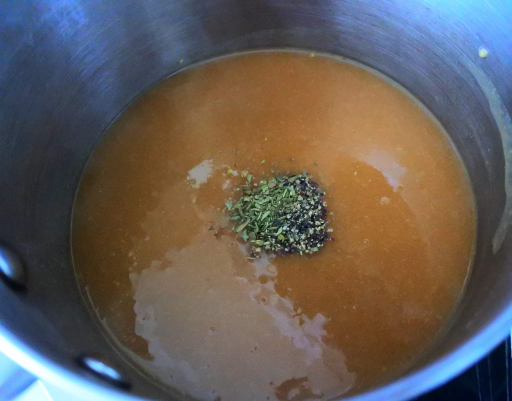 An overhead image of a pot of gravy with black pepper and Italian seasoning added to it.