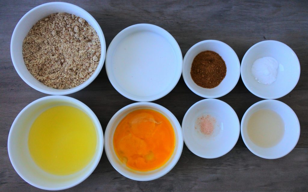 An overhead image of bowls containing individual ingredients for almond flour pancakes including almond flour, separated eggs, coconut milk, coconut sugar, salt, vanilla extract, and baking soda
