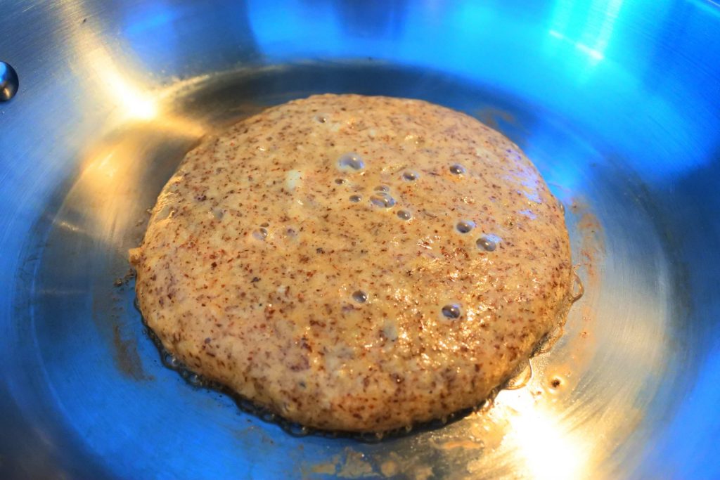 An angled head on image of an unflipped almond flour pancake being cooked in a pan