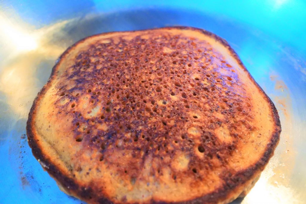An angled head on image of a flipped almond flour pancake being cooked in a pan