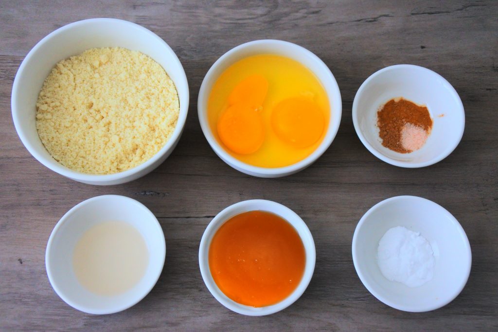 An overhead image of bowl containing the following ingredients: almond flour, eggs, vanilla extract, honey, baking soda, cinnamon powder, nutmeg, and salt,