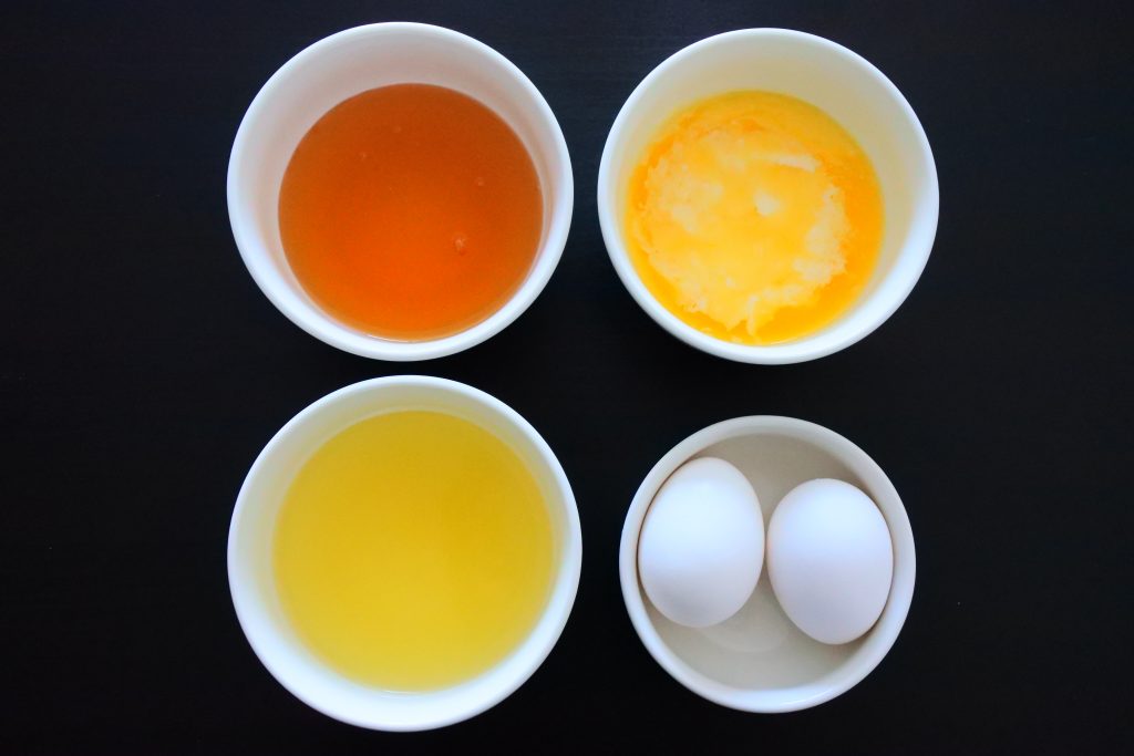 An overhead image of four bowls containing honey, melted butter, pineapple juice and eggs
