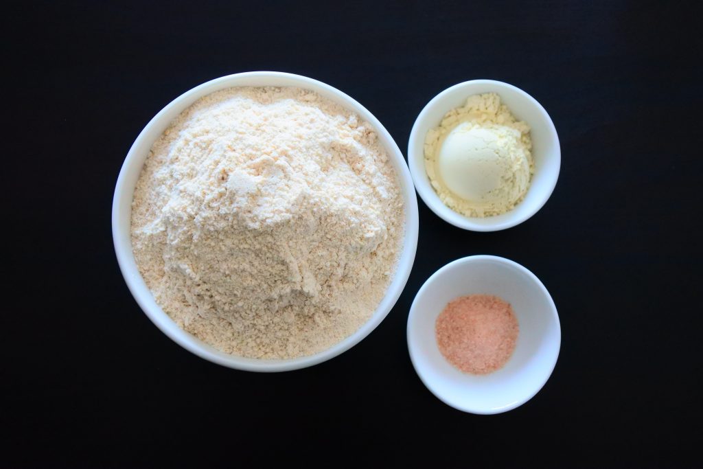 An overhead image of three bowls containing whole wheat flour, vital wheat gluten and salt