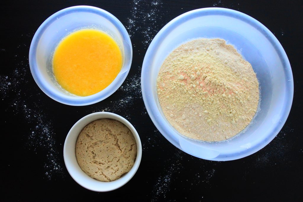 An overhead image of three bowls: one containing whole wheat flour, vital wheat gluten and salt, the other containing activated yeast and the third containing egg, honey, pineapple juice and melted butter