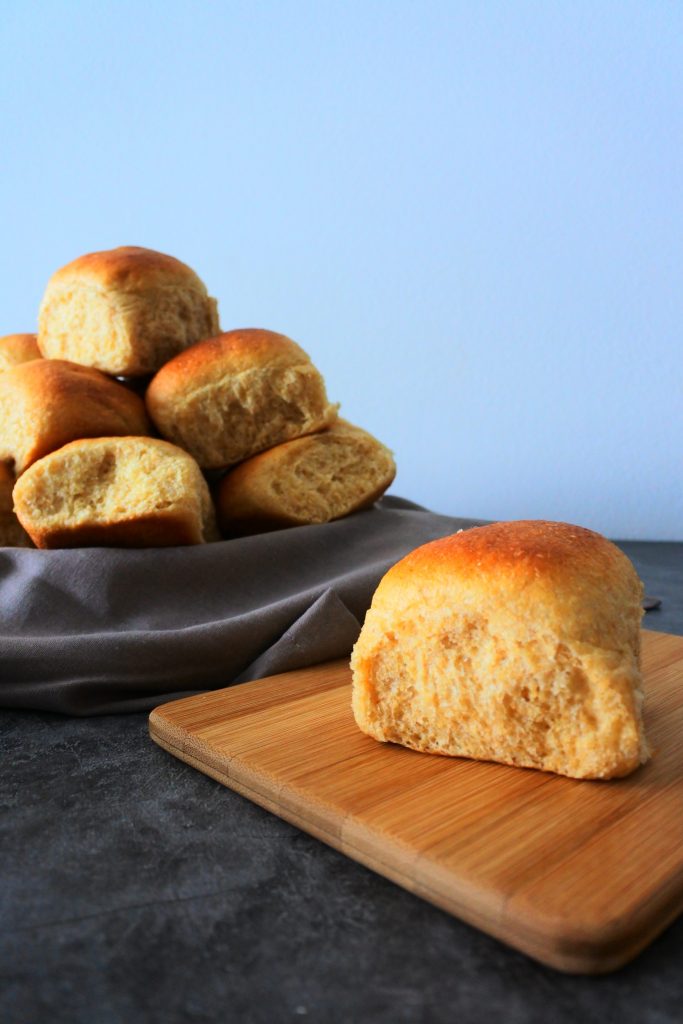 A head on image of a Hawaiian sweet dinner toll on a wooden board with a basket of rolls in the background