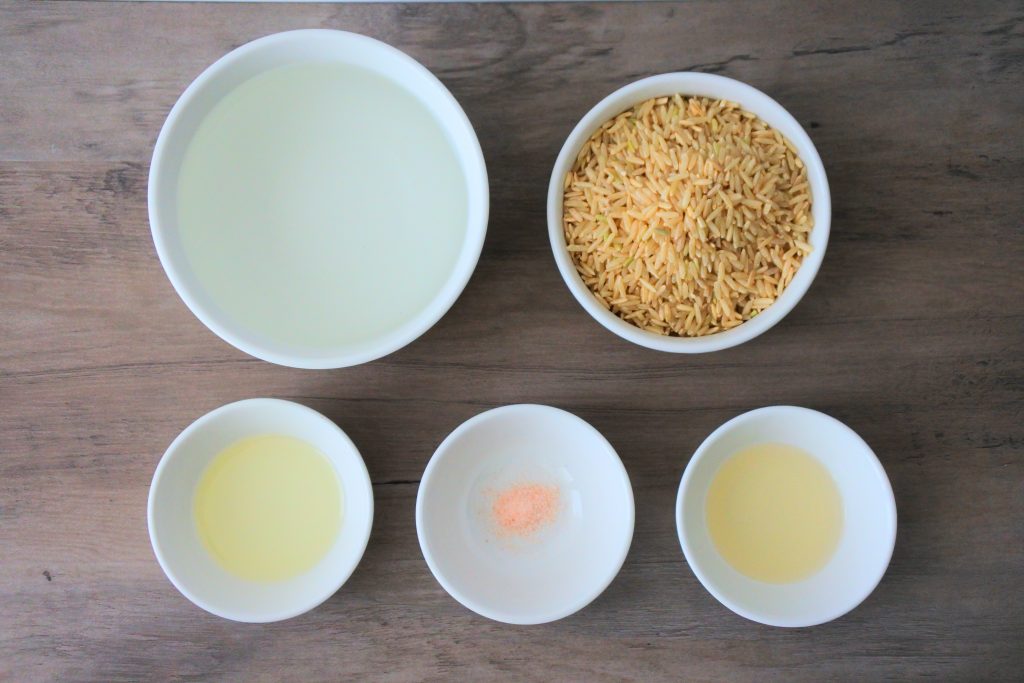 An overhead image of five bowls containing the following ingredients: water, rice, rice wine vinegar, salt, and oil.