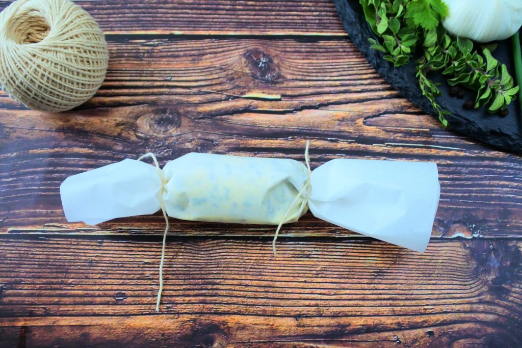 An overhead image of parchment paper wrapped herbed butter tied off with twine