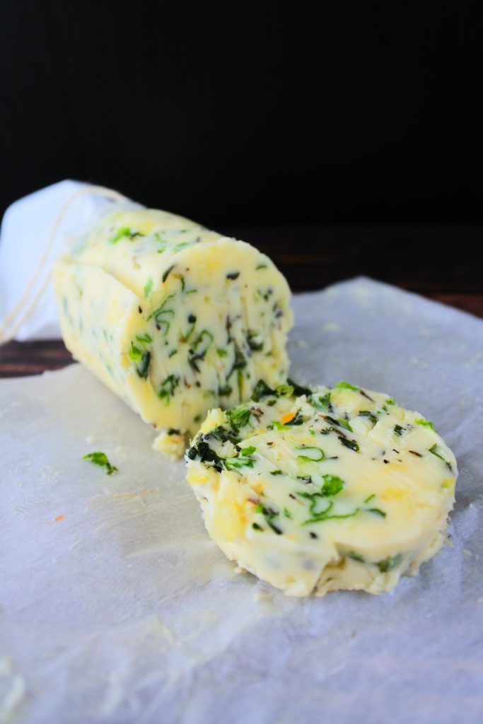 A close up image of sliced herbed butter on a sheet of parchment paper