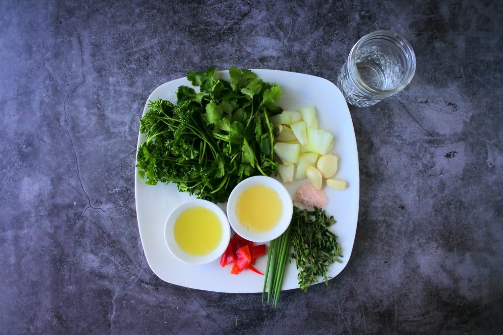 An overhead image of a plate of ingredients for a green seasoning including fresh herbs and spices