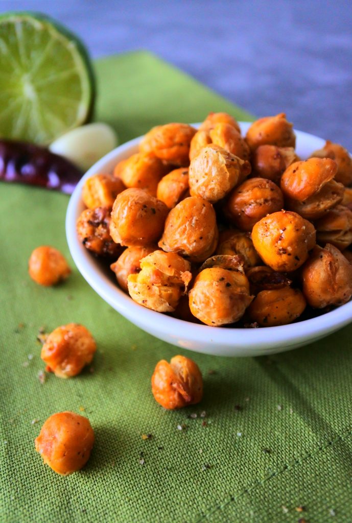 An angled overhead image of a dish of crunchy oven roasted chickpeas on a green linen napkin with spices and seasonings in the background