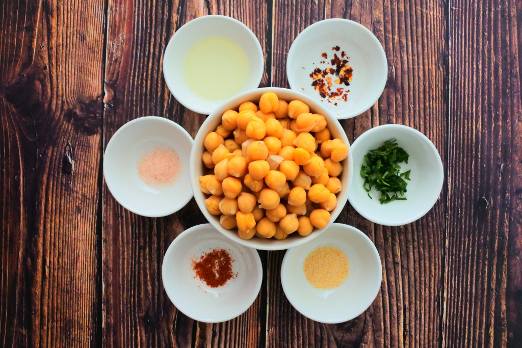 An overhead image of bowls containing ingredients for oven roasted chick peas including: Chickpeas, finely chopped cilantro, garlic powder, cayenne pepper, salt, light olive oil and red pepper flakes