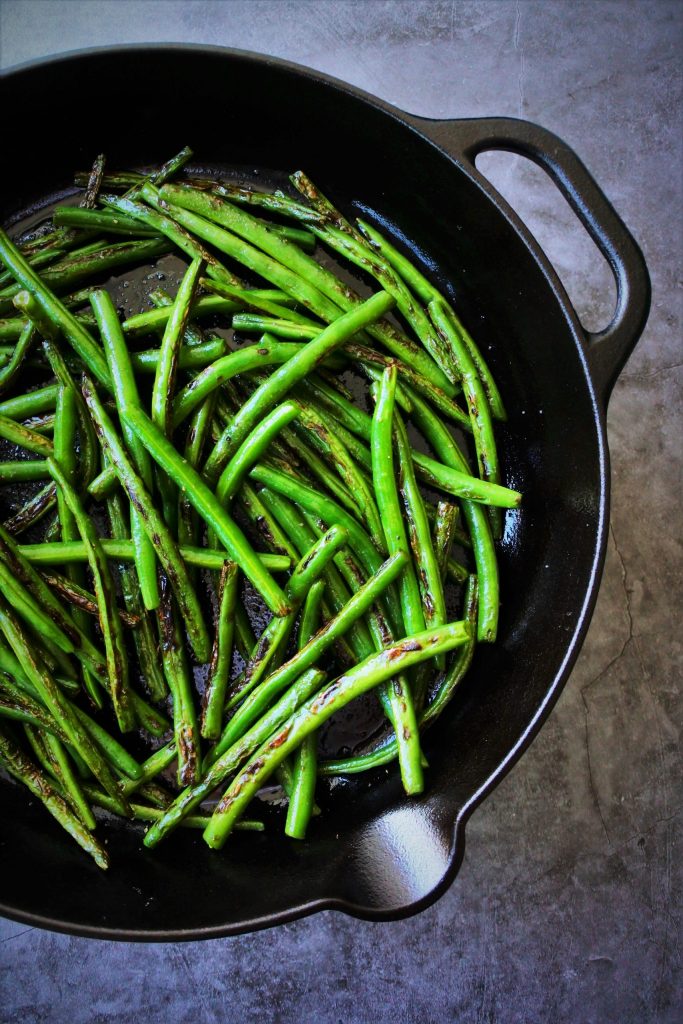 An overhead image of a part of a cast iron skillet of charred green beans