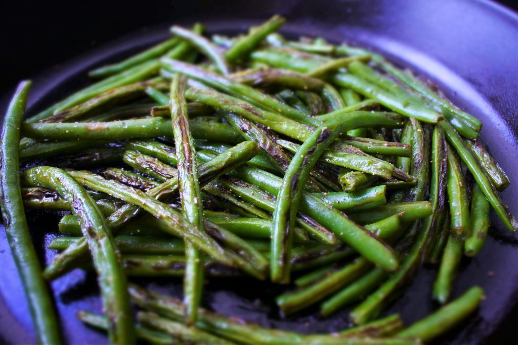 A close up image of charred green beans in a cast iron skillet