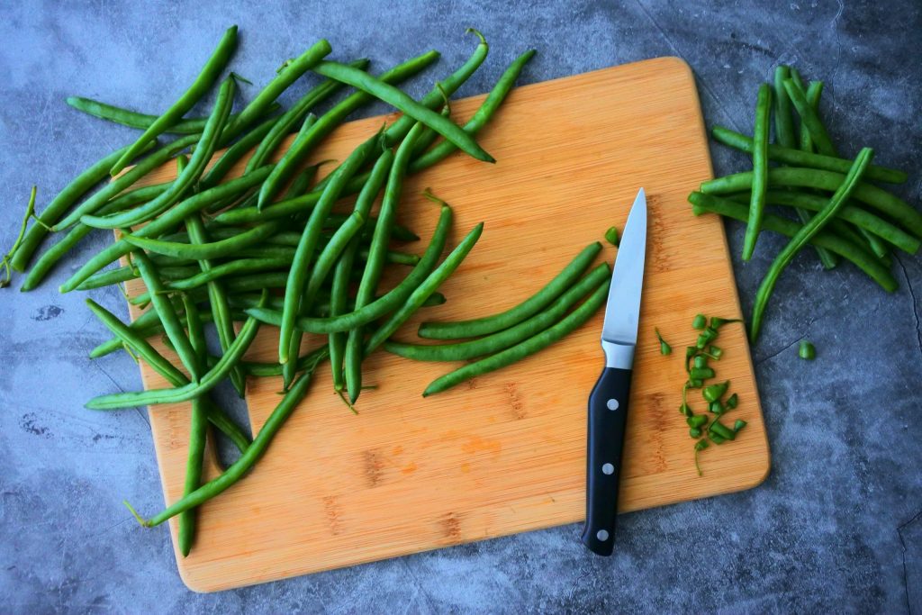 An overhead image of green beans being prepped and their tips being cut off.