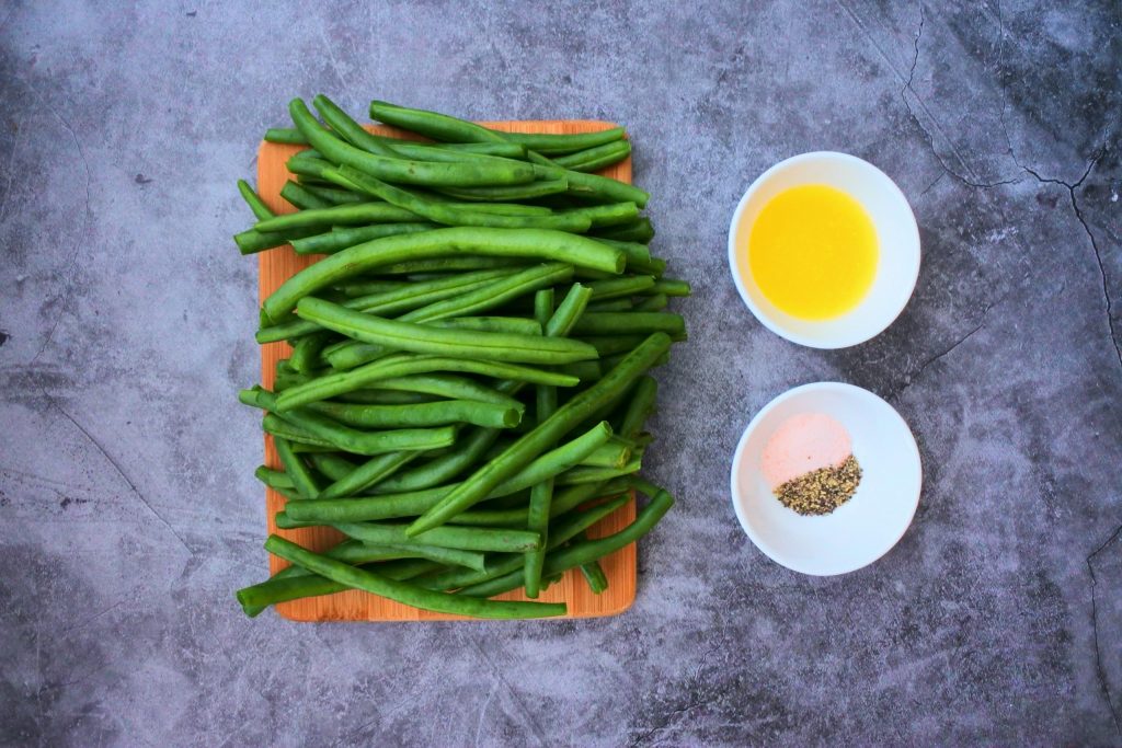 An overhead image of ingredients needed for skillet charred green beans including green beans, melted butter, salt and pepper.
