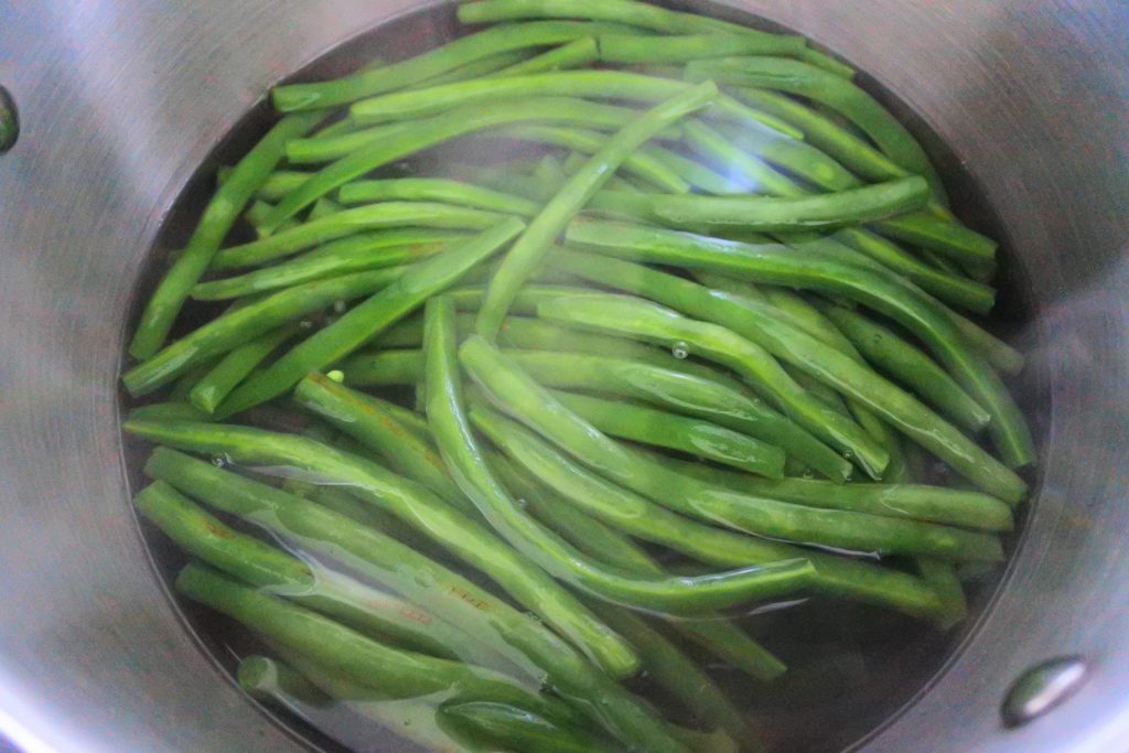 An overhead image of green beans in a pot of boiling water