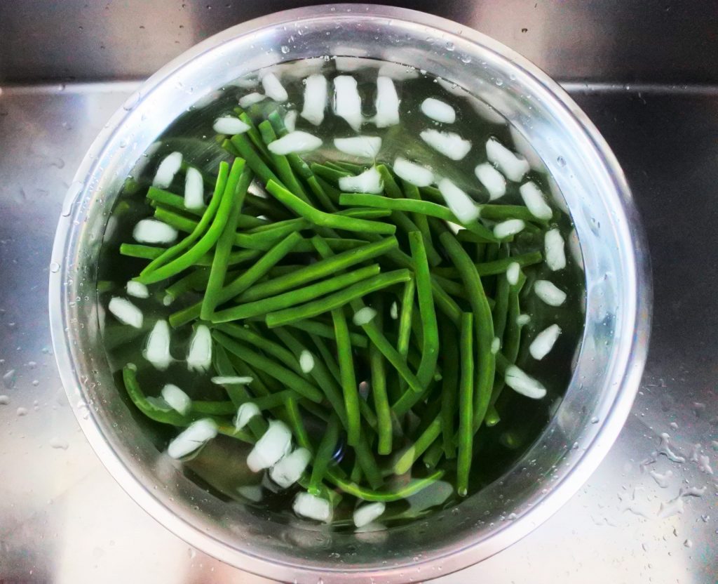 An overhead image of green beans sitting in an ice bath