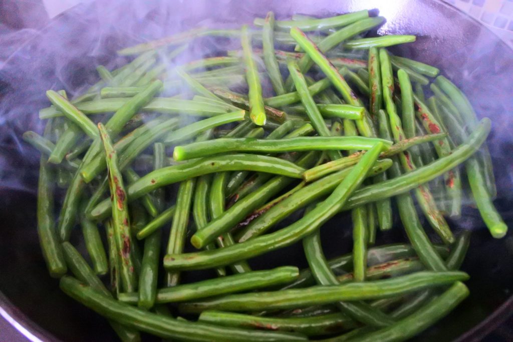 An angled image of smoky green beans in a cast iron skillet