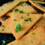A head on image of a pile of cheesy chickpea crackers topped with coarse salt and fresh parsley