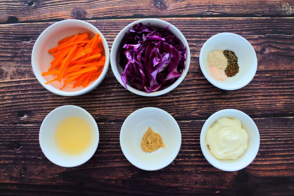 An overhead image of bowls of ingredients for a simple slaw including carrots, red cabbage, spices, mayonnaise, stone ground mustard and lemon juice