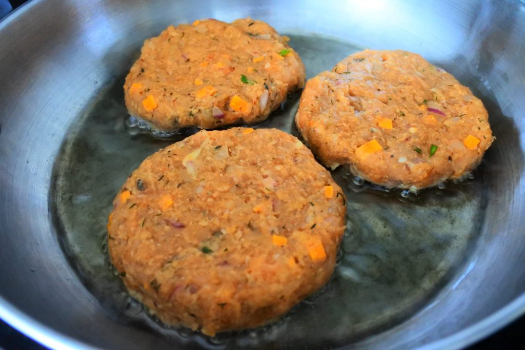 A close up image of three chicken patties being cooked in an oiled pan