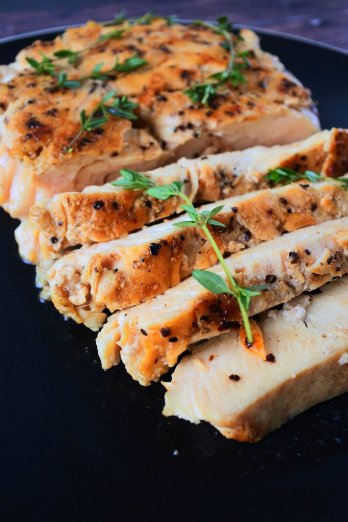 A close up image of sliced pan seared chicken breast topped with fresh thyme sprigs