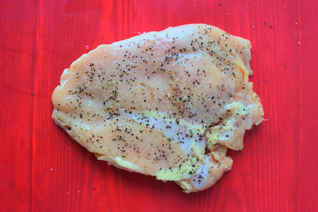 An overhead image of a pounded chicken breast seasoned with salt and pepper