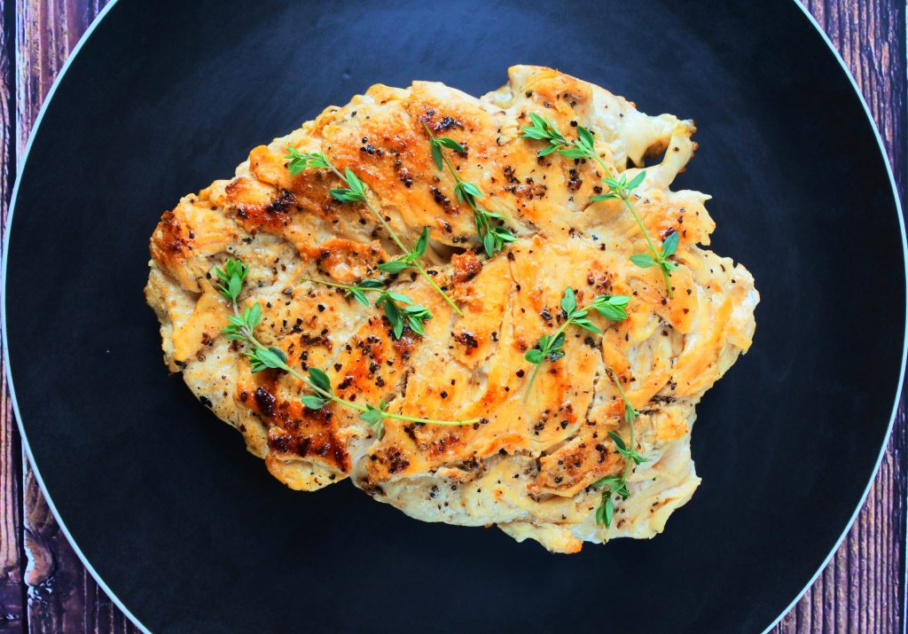 An overhead image of sliced pan seared chicken breast topped with fresh thyme sprigs