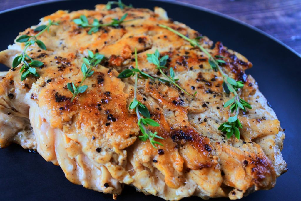 A close up image of sliced pan seared chicken breast topped with fresh thyme sprigs