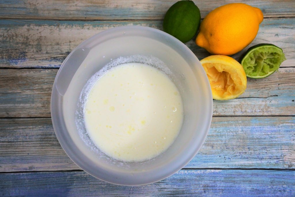 An overhead image of a bowl of homemade buttermilk with some lemons and limes in the top right corner